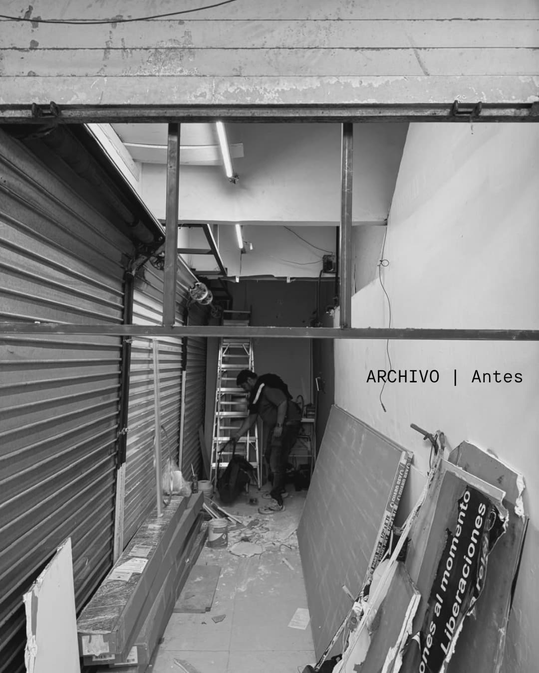Hombre trabajando en un local comercial en remodelación con cortinas metálicas y materiales de construcción.