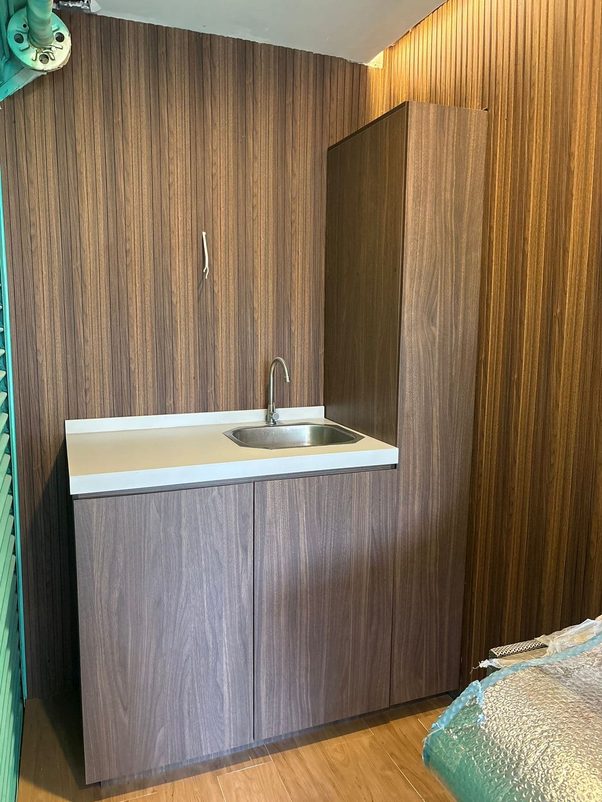 Fregadero de acero inoxidable en encimera blanca con gabinetes de madera y pared listonada.