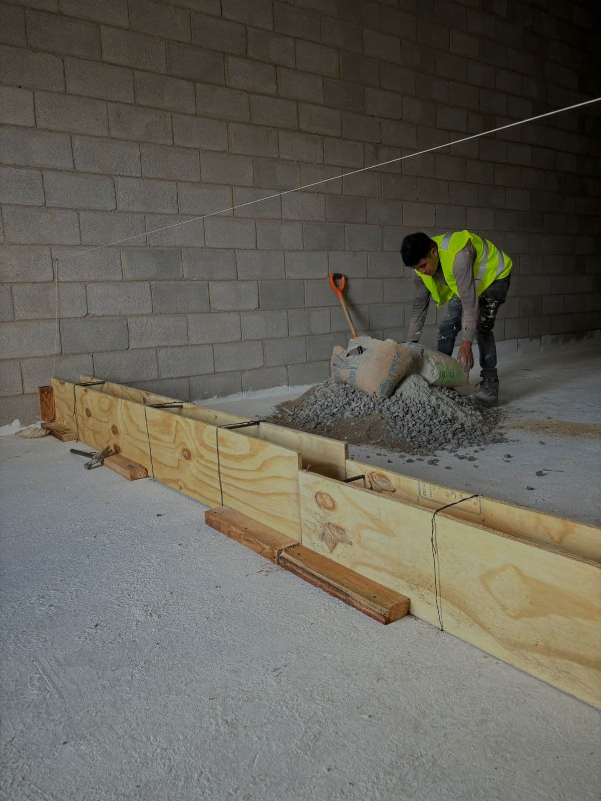 Trabajador con chaleco reflectante prepara mezcla de concreto junto a moldes de madera interiores.